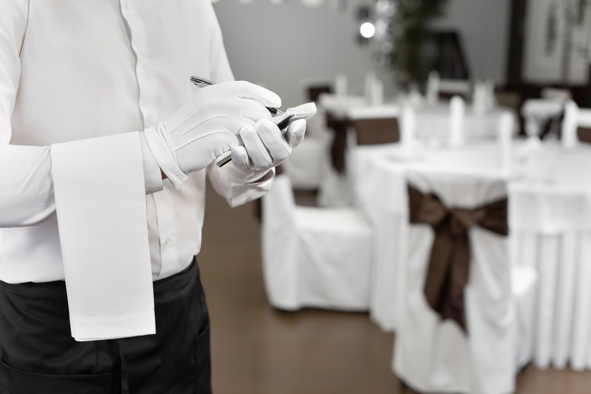 Waiter in a white shirt and bow tie writing down an order in a cafe, close up.